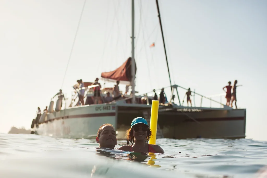 Two people swimming in the water with a boat in the background